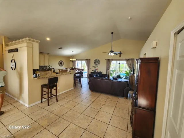 Living room featuring lofted ceiling, light tile patterned floors, and ceiling fan with notable chandelier