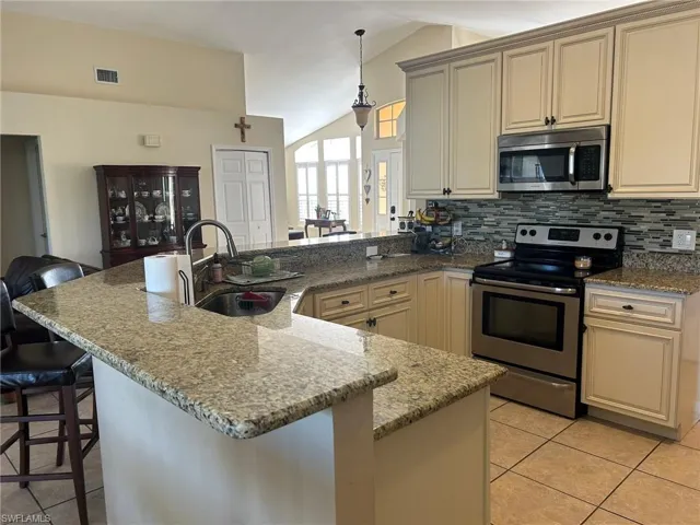 Kitchen with sink, a breakfast bar, stainless steel appliances, vaulted ceiling, and cream cabinetry