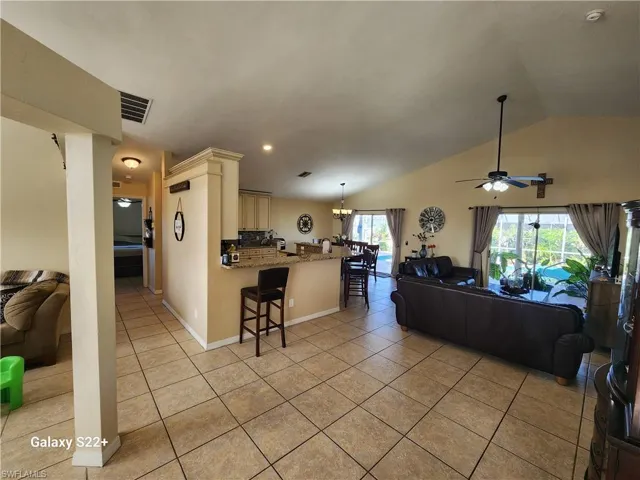 Tiled living room with lofted ceiling and ceiling fan with notable chandelier