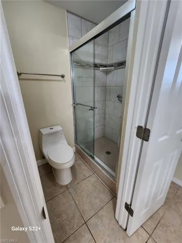 Bathroom with tile patterned floors, toilet, and a shower with door
