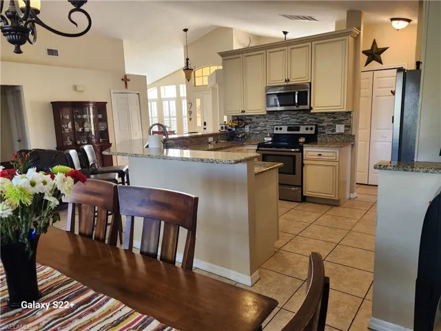 Kitchen featuring hanging light fixtures, vaulted ceiling, cream cabinetry, and appliances with stainless steel finishes