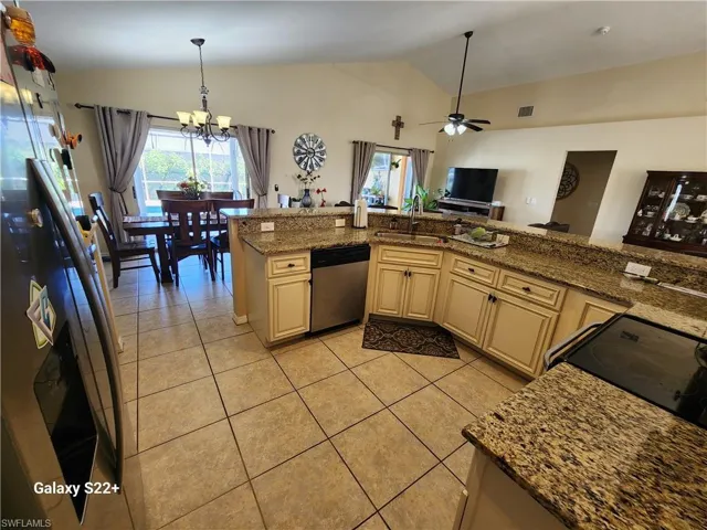 Kitchen featuring lofted ceiling, sink, stone countertops, stainless steel dishwasher, and cream cabinetry