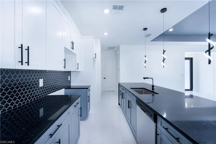 Kitchen with hanging light fixtures, sink, dishwasher, and dark stone counters