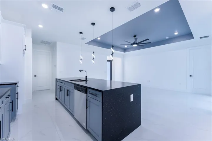Kitchen featuring decorative light fixtures, dishwasher, ceiling fan, a raised ceiling, and an island with sink