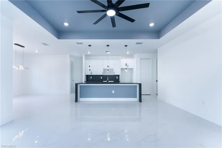 Kitchen with tasteful backsplash, decorative light fixtures, a raised ceiling, light tile floors, and white cabinets