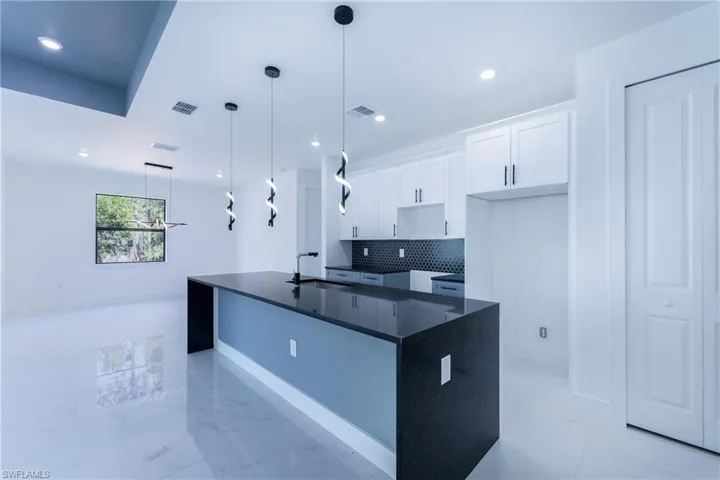 Kitchen with a kitchen island with sink, backsplash, pendant lighting, sink, and light tile flooring