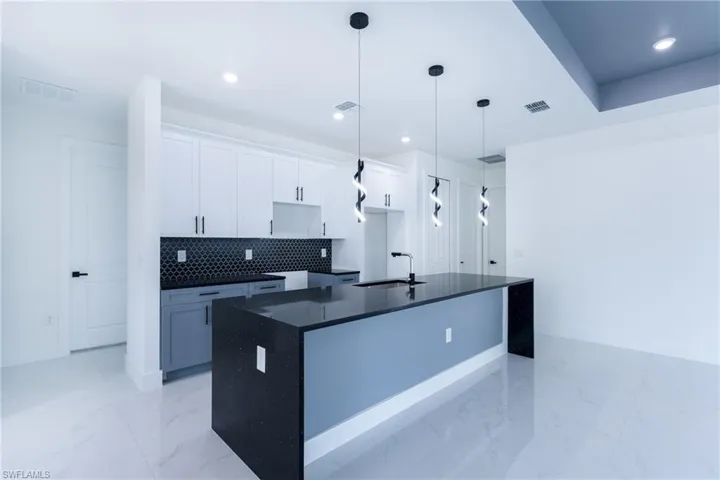Kitchen featuring tasteful backsplash, a center island with sink, light tile floors, sink, and white cabinets