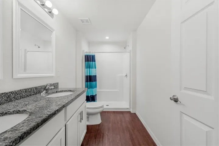 Full bath with a shower stall, double vanity, and dark wood-style floors