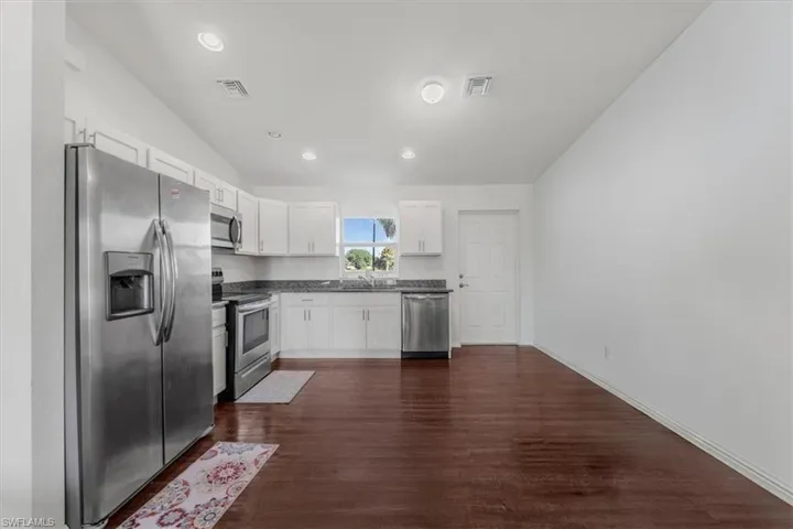 Kitchen featuring appliances with stainless steel finishes, lofted ceiling, dark wood-type flooring, white cabinetry, and recessed lighting