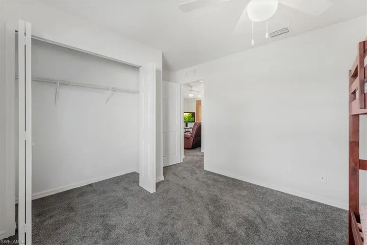 Unfurnished bedroom featuring dark carpet, ceiling fan, and a closet