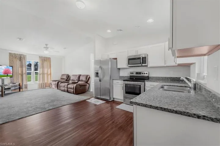 Kitchen featuring dark stone countertops, white cabinetry, vaulted ceiling, stainless steel appliances, and open floor plan