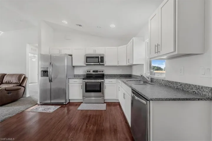 Kitchen with stainless steel appliances, vaulted ceiling, white cabinets, dark wood-style floors, and recessed lighting