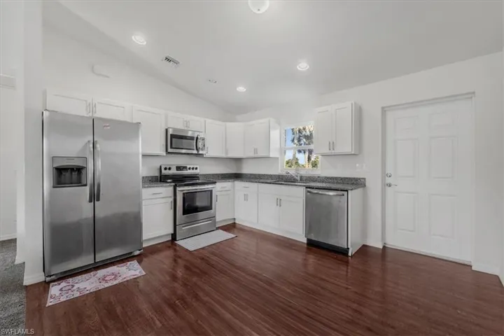 Kitchen with stainless steel appliances, vaulted ceiling, white cabinetry, dark wood-style flooring, and recessed lighting