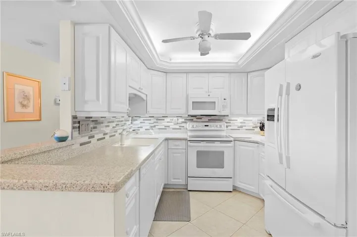 Kitchen featuring white appliances, sink, ceiling fan, and white cabinets