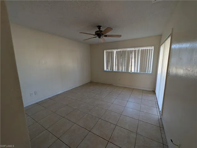 Empty room with a textured ceiling, a ceiling fan, and light tile patterned floors
