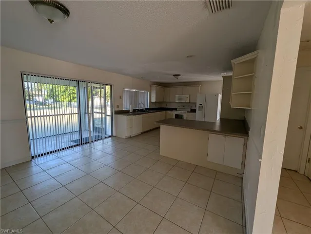 Kitchen with a peninsula, dark countertops, white appliances, light tile patterned flooring, and open shelves