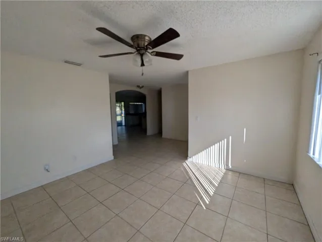 Empty room featuring arched walkways, a textured ceiling, light tile patterned flooring, and ceiling fan
