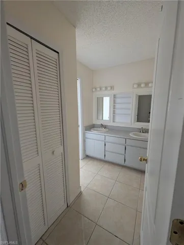 Bathroom with a closet, double vanity, a textured ceiling, and light tile patterned floors