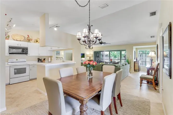 Open-concept living space featuring a dining area with a chandelier, a kitchen with white cabinetry and appliances, and a living room with exterior access