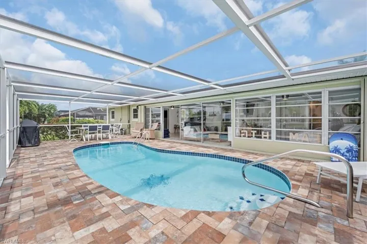 Outdoor pool with a sunroom, glass enclosure, a patio area, and a grill