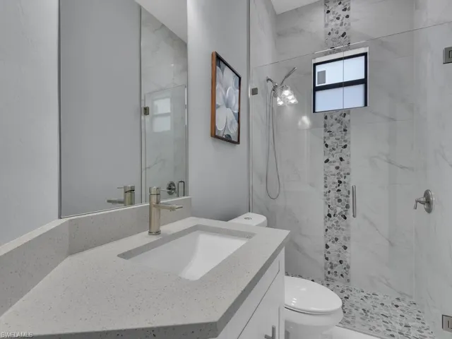 Full bath with a marble finish shower, vanity, and toilet