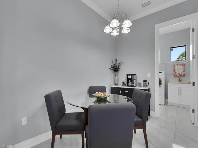 Dining space featuring a chandelier, washer / dryer, baseboards, ornamental molding, and visible vents