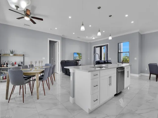 Kitchen featuring marble finish floor, light countertops, a sink, crown molding, and open floor plan