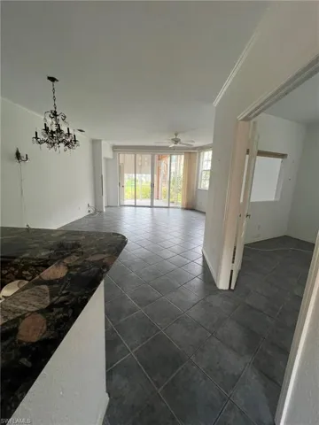 Unfurnished living room with dark tile patterned floors, a ceiling fan, a chandelier, and ornamental molding