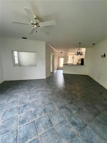 Unfurnished living room featuring crown molding, dark tile patterned floors, a chandelier, and a ceiling fan