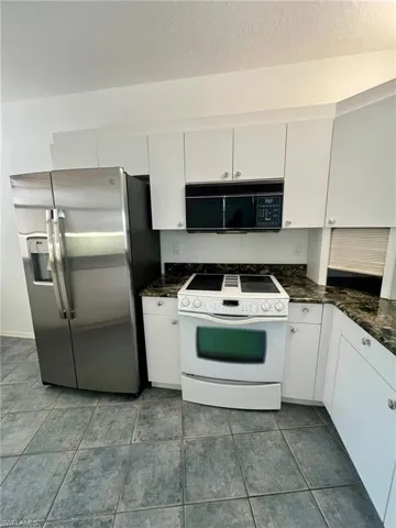 Kitchen featuring white range with electric cooktop, stainless steel refrigerator with ice dispenser, black microwave, white cabinets, and a textured ceiling