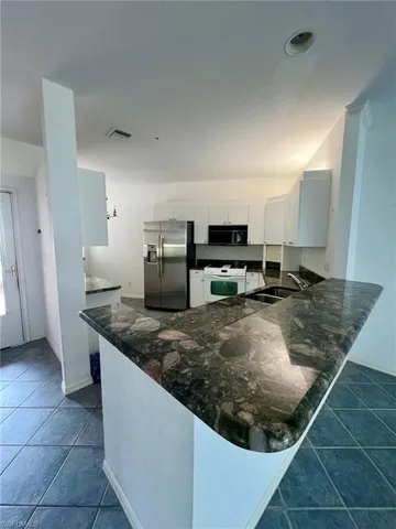 Kitchen featuring a peninsula, stainless steel refrigerator with ice dispenser, dark tile patterned flooring, black microwave, and electric range