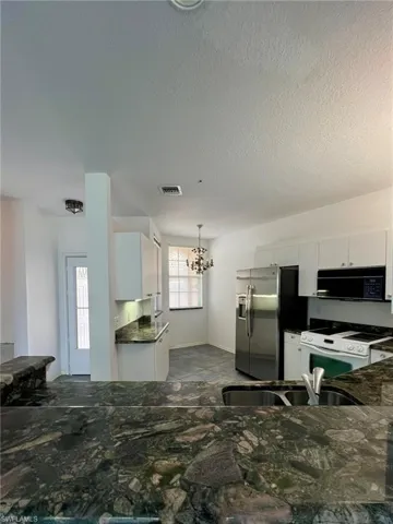 Kitchen with white cabinets, white electric range oven, black microwave, and a textured ceiling