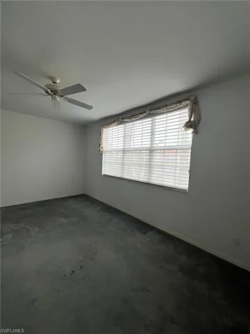Unfurnished room featuring dark colored carpet, a ceiling fan, and a textured ceiling