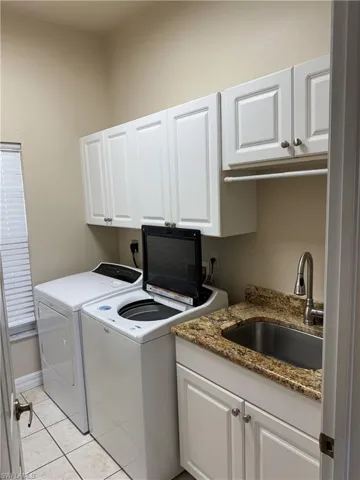 Washroom featuring a sink, light tile patterned floors, cabinet space, and washer and dryer