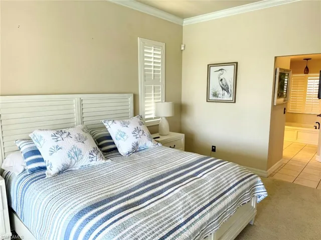 Tiled bedroom featuring ensuite bath, baseboards, and ornamental molding
