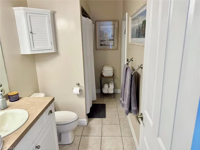 Full bathroom with tile patterned floors, toilet, vanity, a shower with curtain, and baseboards