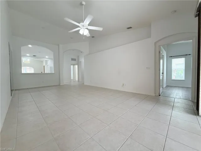 Unfurnished living room featuring arched walkways, light tile patterned floors, ceiling fan, and lofted ceiling