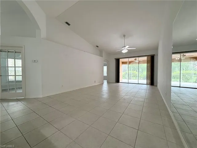 Empty room featuring arched walkways, light tile patterned floors, plenty of natural light, high vaulted ceiling, and ceiling fan