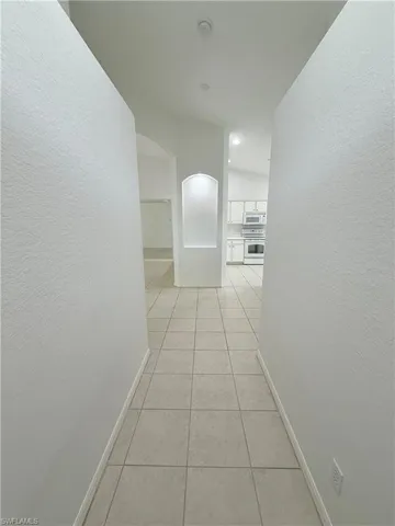 Hallway featuring light tile patterned floors, a textured wall, and arched walkways