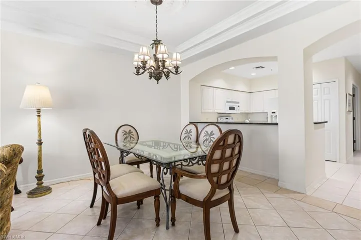 Dining room featuring light tile patterned floors, a raised ceiling, arched walkways, crown molding, and a chandelier