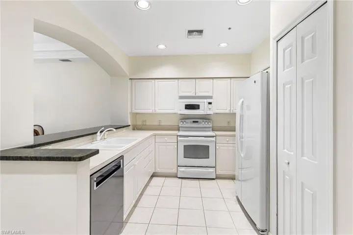 Kitchen featuring white and stainless steel appliances, white cabinetry, raised granite countertop.