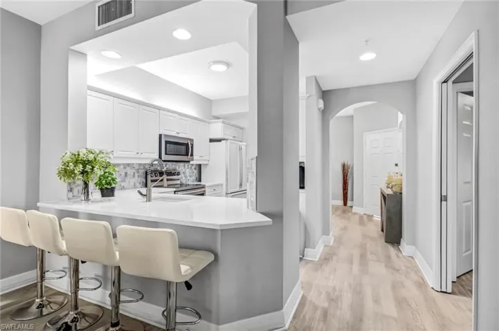 Kitchen with white cabinets, kitchen peninsula, a kitchen breakfast bar, light hardwood / wood-style flooring, and appliances with stainless steel finishes