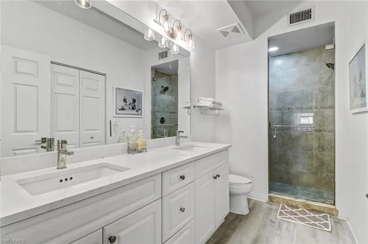 Bathroom with wood-type flooring, a shower with shower door, vanity, and toilet