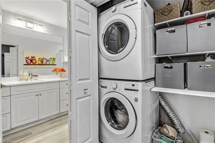 Clothes washing area with stacked washer and clothes dryer and light wood-type flooring