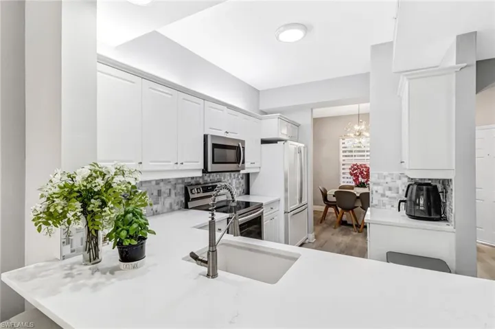 Kitchen with decorative backsplash, stainless steel appliances, a notable chandelier, and sink
