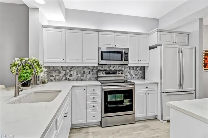 Kitchen featuring decorative backsplash, stainless steel appliances, white cabinetry, and light hardwood / wood-style flooring