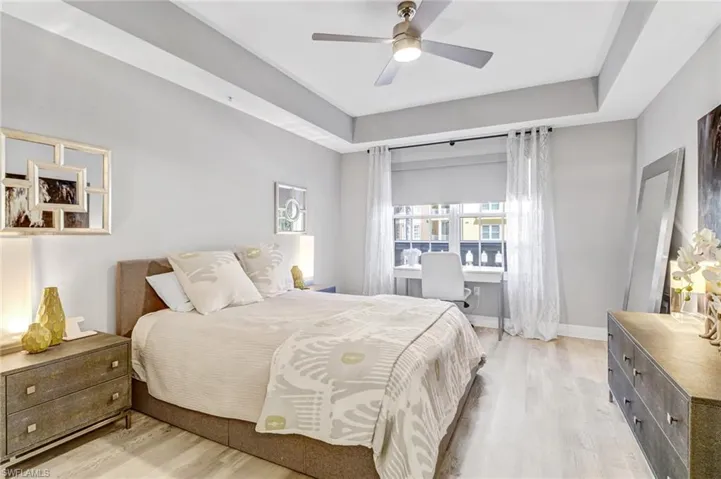 Bedroom with light wood-type flooring, a tray ceiling, and ceiling fan