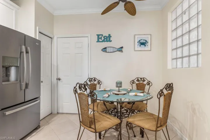 Eat-in Kitchen featuring appliances with stainless steel finishes, sleek white cabinetry, light tile patterned floors, ornamental molding, and light granite counters and backsplash