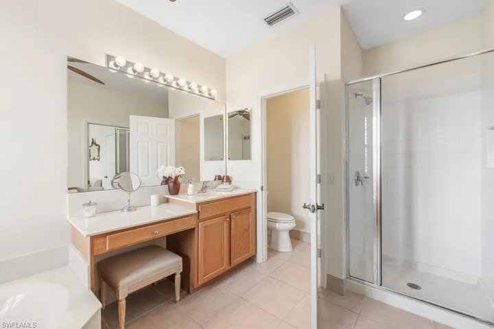 Master Bathroom with a soaking tub bath, two vanities, light tile patterned floors, walk-in shower, ceiling fan, and plantation shutters