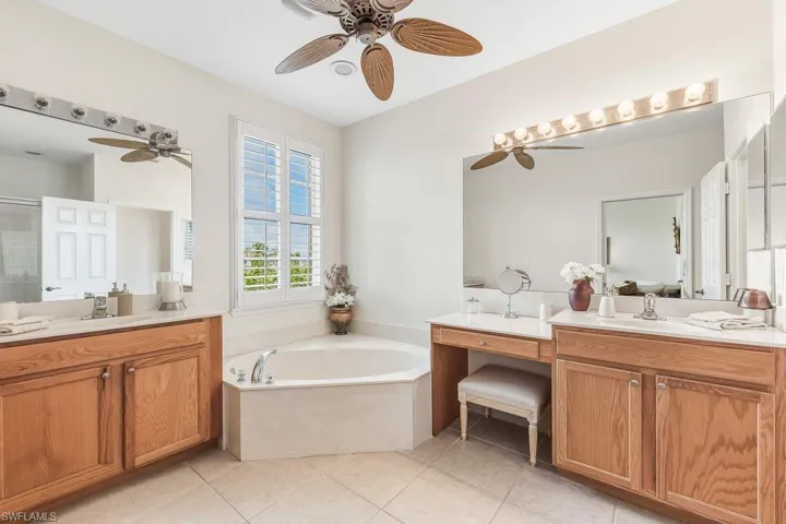 Master Bathroom with a soaking tub bath, two vanities, light tile patterned floors, walk-in shower, ceiling fan, and plantation shutters